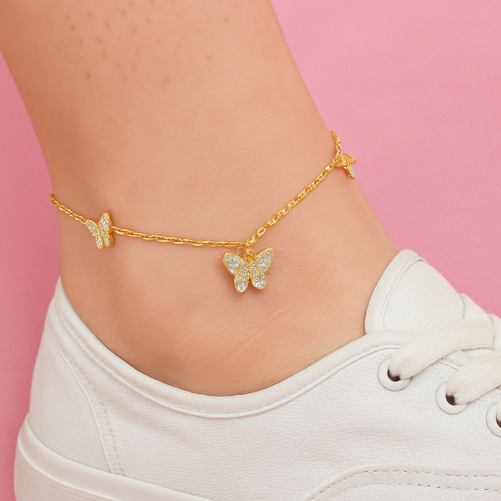 Gold butterfly anklets on a person's ankle against a pink background Gold anklet with butterfly charms on an ankle wearing a white sneaker, set against a pink background