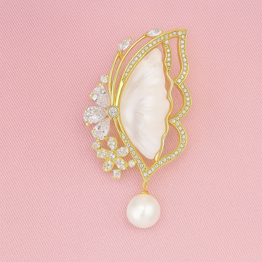 Decorative brooch with pearl and gemstones on a pink background Elegant butterfly-shaped brooch with mother-of-pearl inlay, gold trim, and crystal accents on a white background
