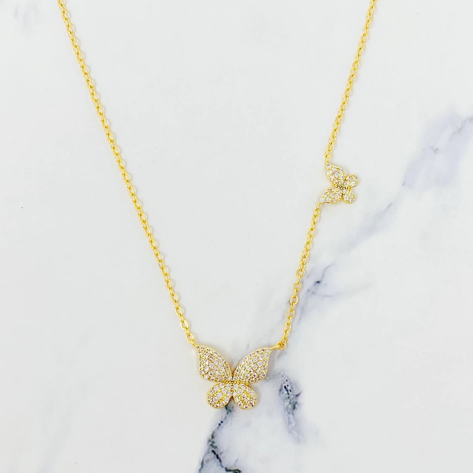 Gold butterfly necklace on a marble surface “Delicate gold necklace with crystal butterfly pendants displayed on a white marble surface”
