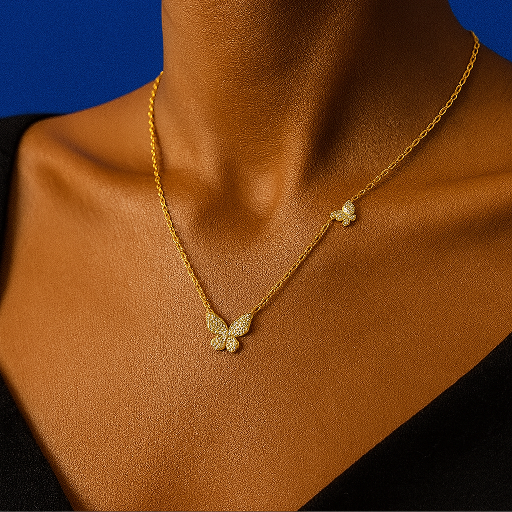 Gold necklace with butterfly pendants on a mannequin against a blue background “Elegant gold necklace with two butterfly pendants worn on a mannequin against a deep blue background”
