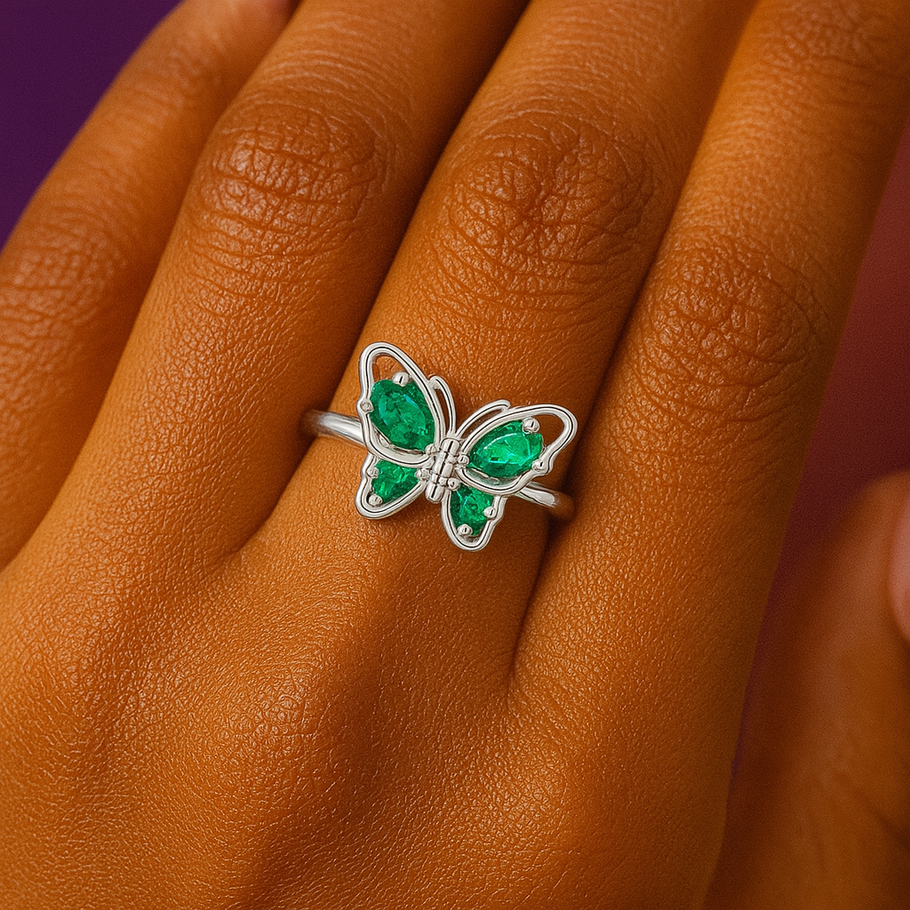 “Elegant silver butterfly ring with green emerald-like gemstones on a woman's finger against a warm background”
