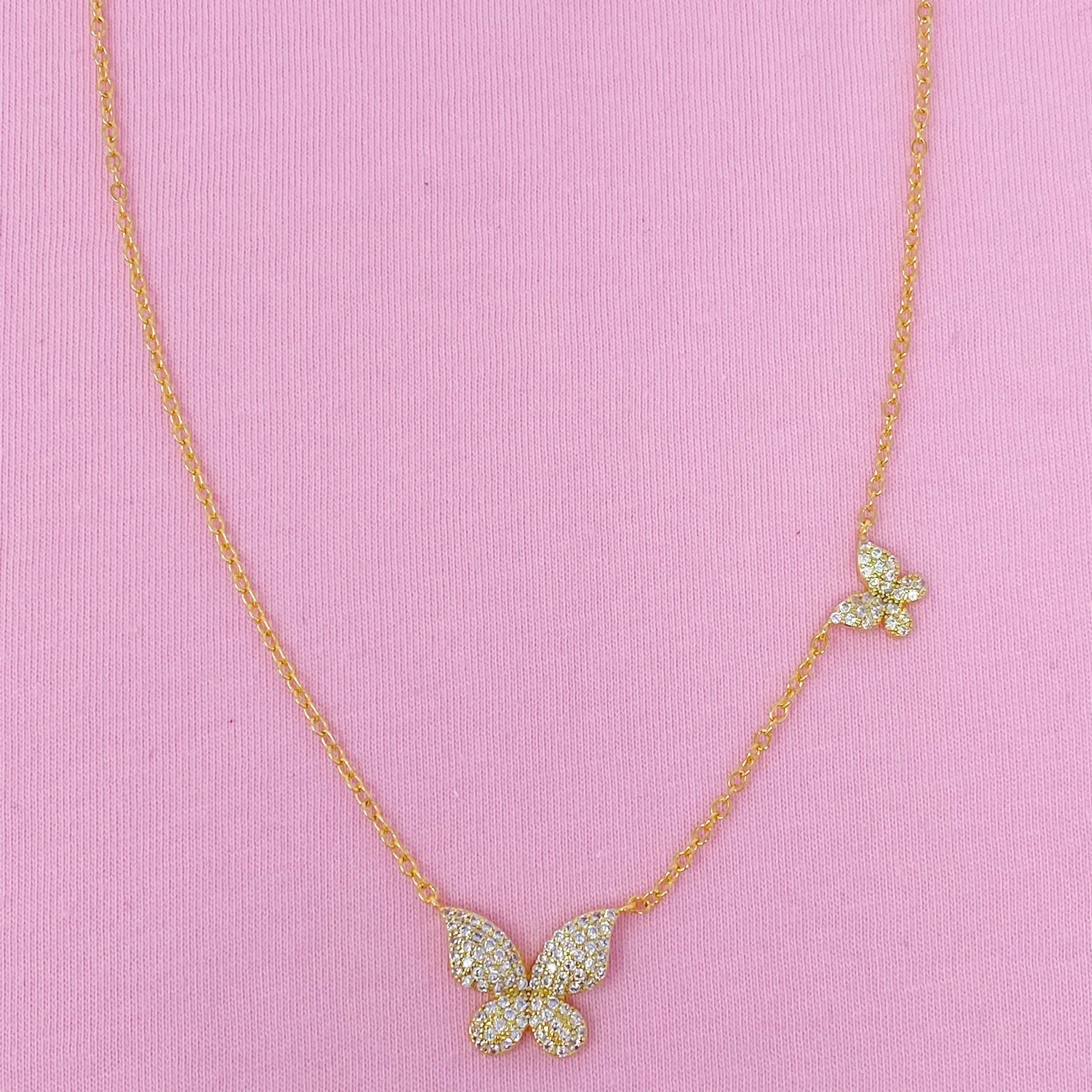 Butterfly necklace with gemstones on a pink background “Elegant gold butterfly necklace with crystal accents displayed on a soft pink fabric background”
