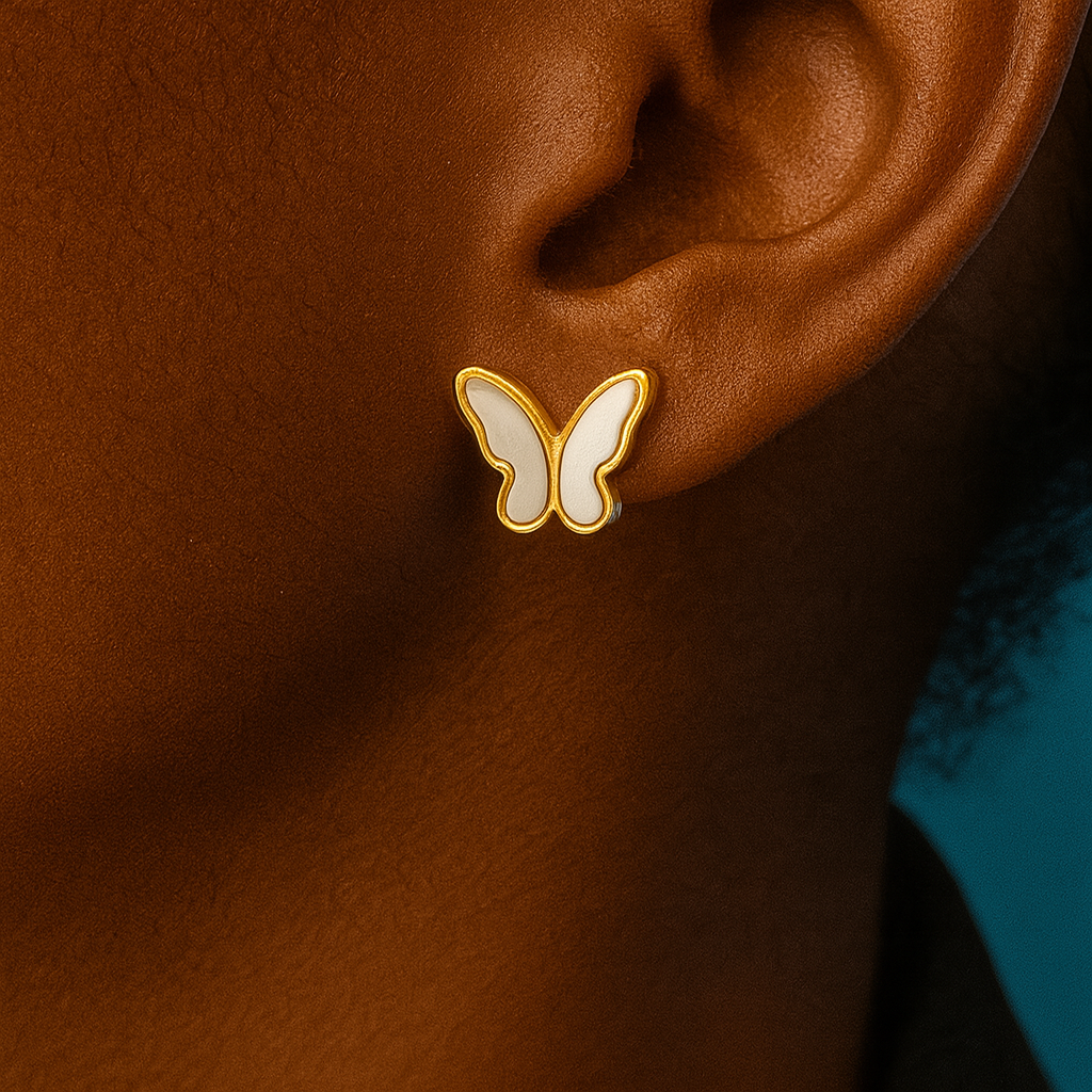 Butterfly-shaped earring on an ear with a blurred background Close-up of a white butterfly stud earring with gold trim worn on an ear, teal background
