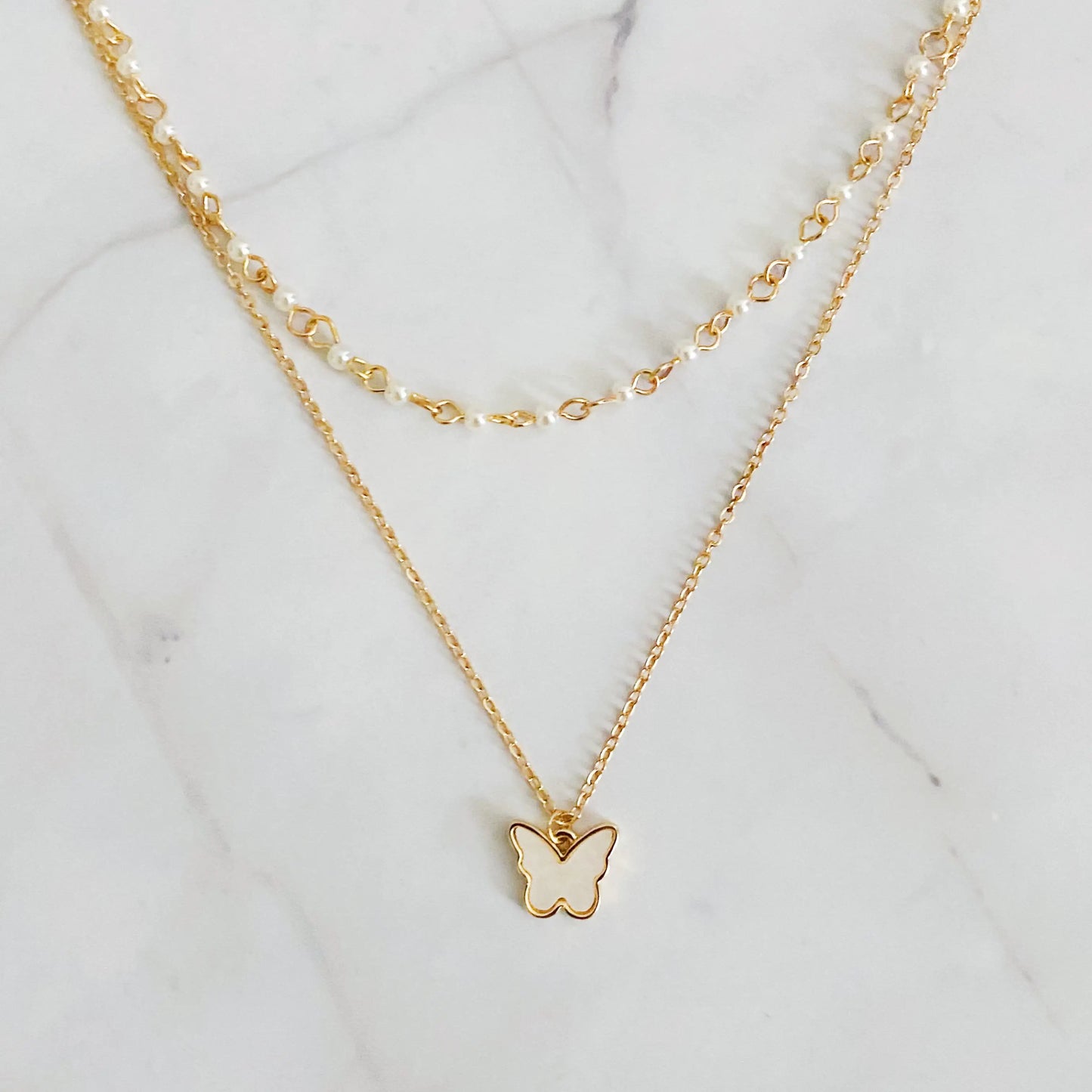 Gold butterfly necklace with pearl chain on a marble background "Delicate gold butterfly pendant necklace with pearl chain on a white marble background"
