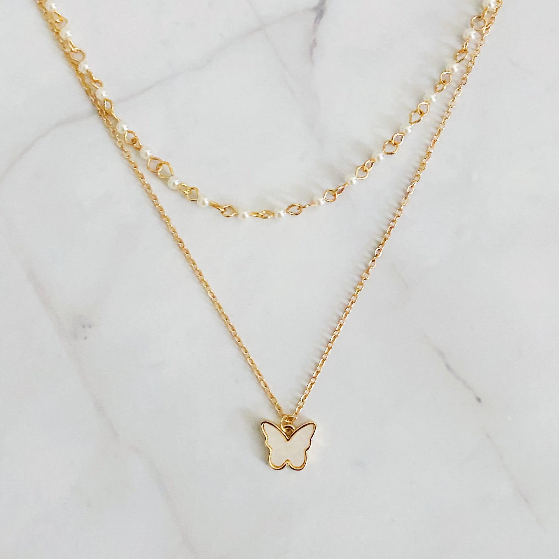 Gold butterfly necklace with pearl chain on a marble background "Delicate gold butterfly pendant necklace with pearl chain on a white marble background"
