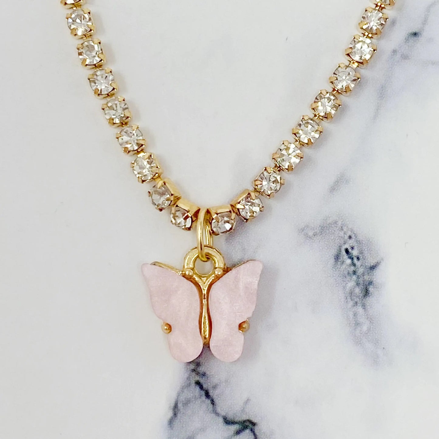 Necklace with a pink butterfly pendant on a marble background “Close-up of a gold necklace with a pink rose quartz butterfly pendant, placed on a marble background”
